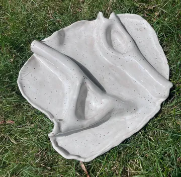 Ceramic sculpture resting on grass outdoors.