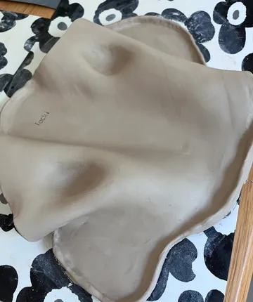Tonfigur liegt auf blumigem Tisch.