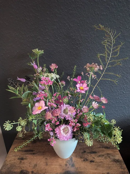 Blumenarrangement in weißer Vase auf Holztisch.