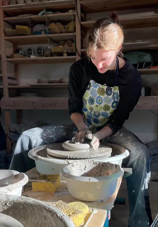 Person shaping clay on a pottery wheel.