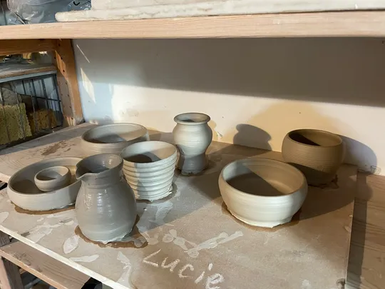 Clay pots drying on a wooden shelf.