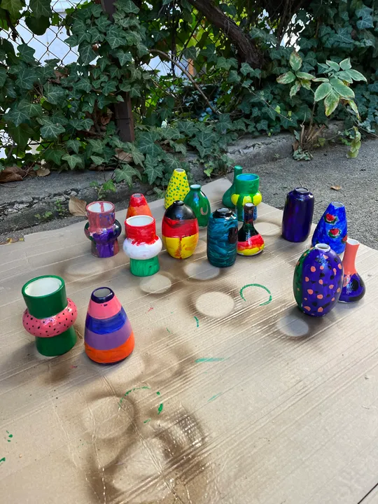 Colorful painted jars drying on cardboard outside.