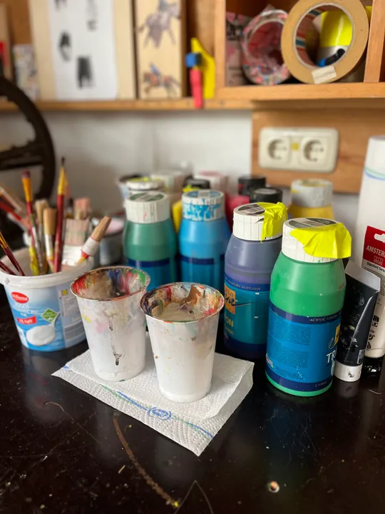 Paints and brushes on cluttered art desk.