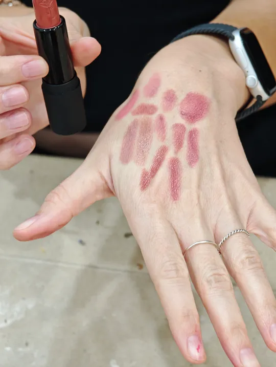 Hand trägt Lippenstiftproben auf Handrücken auf.