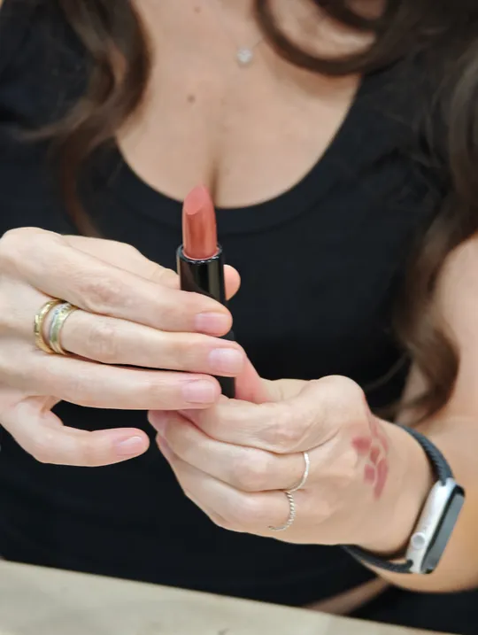 Hände halten Lippenstift, dunkles Shirt sichtbar.