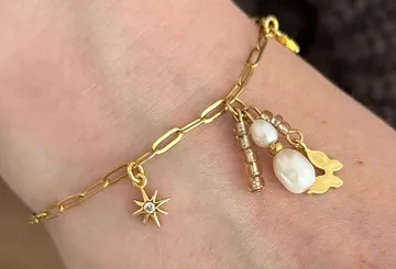 Goldenes Armband mit Anhängern und Perlen am Handgelenk.