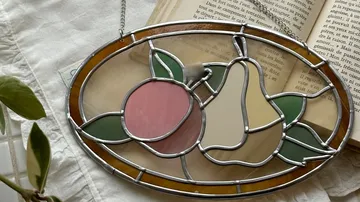 Früchte aus Buntglas auf offenem Buch.