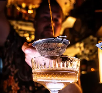 Bartender straining cocktail into glass at bar.