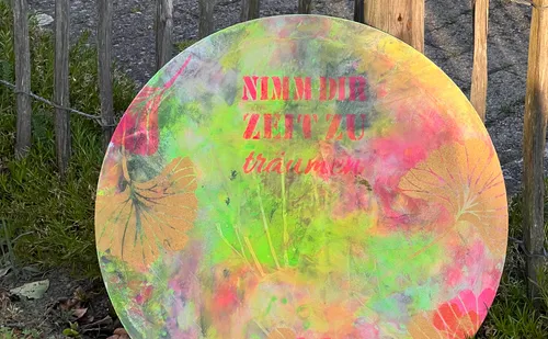 Colorful circular sign in garden, reads in German.