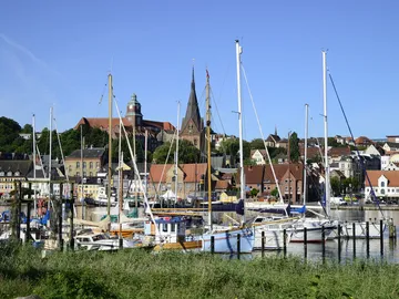Sailing boats in the harbor, surrounded by houses and mountains.