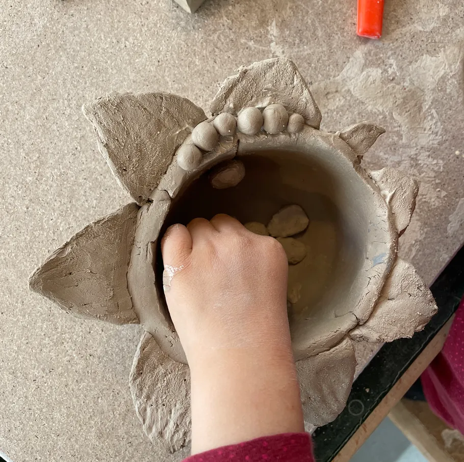 Child molding pottery on a wooden table.
