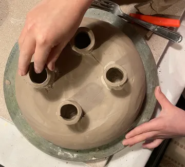 Hands shaping clay sculpture on table.