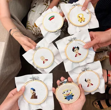 Hands holding various embroidered hoops, showcasing artworks.