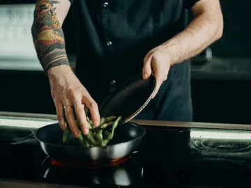 Boiling hand places vegetables in a pan on the stovetop.