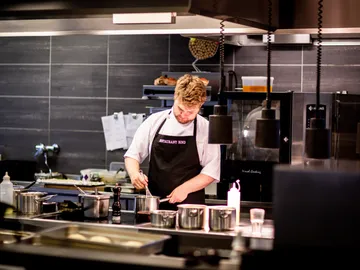 Cook stirs in pots in a modern restaurant kitchen.