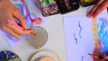 Hände malen auf Papier mit Pinseln.