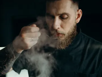 A man with a beard is trying steaming food in a dark room.
