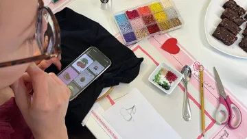 Person stickt mit Smartphone-Anleitung.