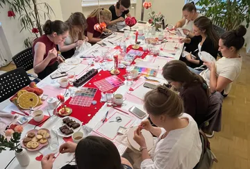 Frauen sticken an einem großen, dekorierten Tisch.