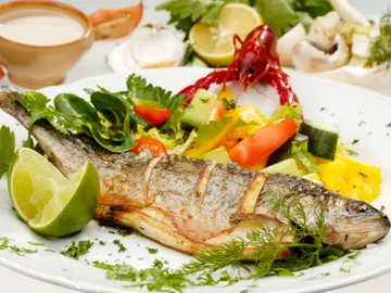 Gegrillter Fisch liegt auf einem Teller mit Gemüse.