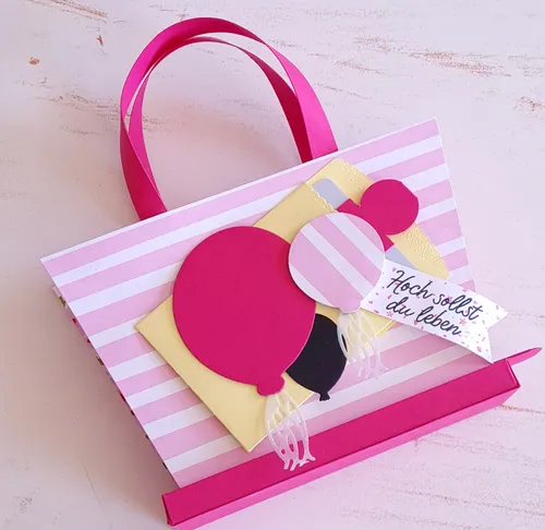 Geschenktasche mit Ballons auf gestreiftem Hintergrund.