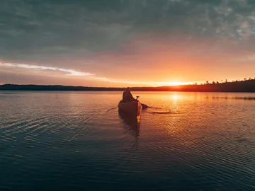 Kanu fährt über den ruhigen See bei Sonnenuntergang.