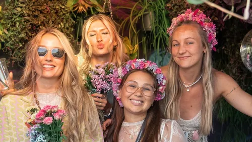Vier Frauen lächeln mit Blumenkronen im Freien.