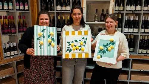 Three women holding lemon paintings in store.