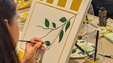 Person painting leaves on a canvas indoors.