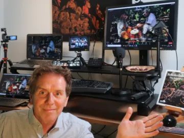 Mann sitzt vor Computerbildschirmen und zeigt mit der Hand.