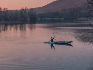 Ein Kajakfahrer paddelt ruhig auf einem spiegelnden Wasser.