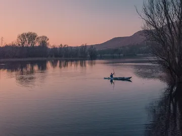 Ein Kajakfahrer paddelt auf einem ruhigen See bei Sonnenuntergang.