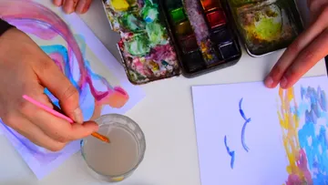 Hände malen mit Aquarellfarben auf Papier.