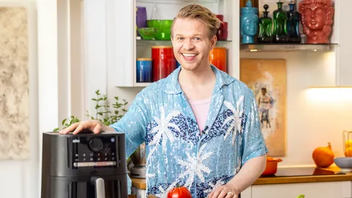 Person lächelnd, benutzt Heißluftfritteuse, in Küche.