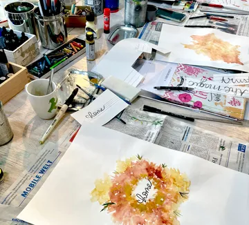 Art supplies and paintings on cluttered desk.
