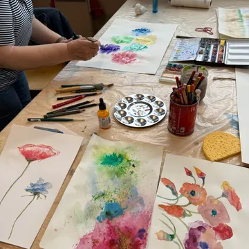 Person painting watercolor flowers on table.