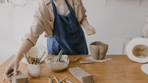 Person shaping clay on wooden table.