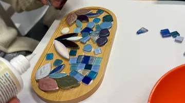 Mosaikfliesen werden auf Holzbrett arrangiert.