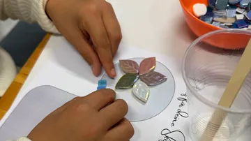 Hände ordnen Mosaikfliesen auf Papier an.