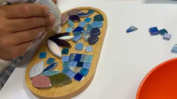 Hand klebt Fliesen auf Holzunterlage.