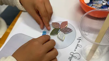 Hände ordnen Glasfliesen auf Papier.