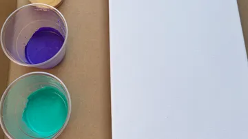 Purple and teal paint cups near blank canvas.