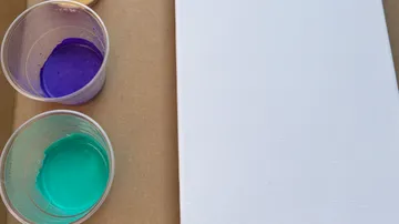 Blank canvas beside cups of paint.