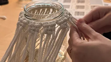 Hände knüpfen Makramee an ein Glasgefäß.