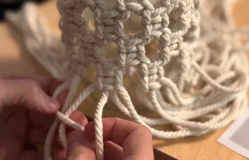 Hände knüpfen Seil in Makramee-Muster.