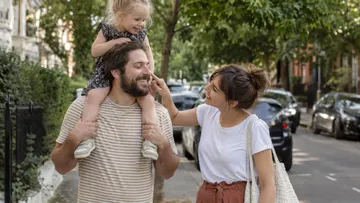 Familie spaziert lachend durch sonnige Straße.