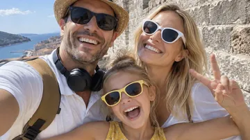 Family smiling, taking selfie by stone wall.