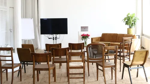 Leere Stühle vor Fernseher und Couch im Raum.