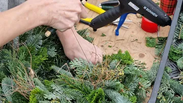 Hände basteln Weihnachtskranz auf Tisch.