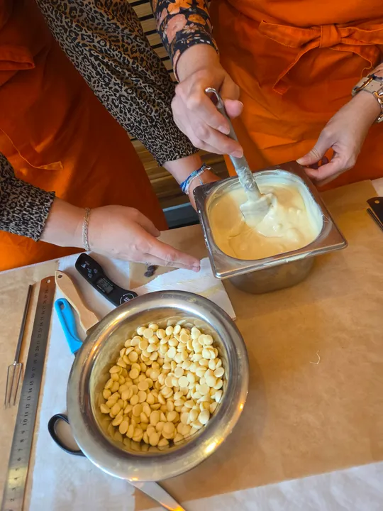 Personen rühren geschmolzene Schokolade am Tisch.